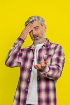 Caucasian middle-aged mature man on yellow background placing hand on forehead, heavy sigh indicating weariness. Disappointment, repeated failures creating visible irritation, comedic facepalm style