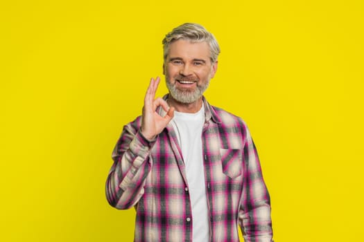 Okay. Happy Caucasian middle-aged man looking approvingly at camera showing ok gesture like sign positive feedback approve something good, celebrate victory. Mature guy on yellow background indoors