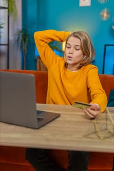 Caucasian teenager boy making an online purchase on laptop at home. Entering credit card information, clicking Order for new game item while sitting on couch by table, feeling satisfied with purchase