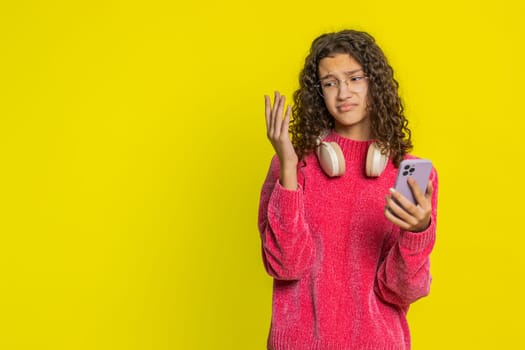 Upset sad Caucasian girl use smartphone typing browsing, play game, loses surprised by sudden lottery results bad fortune loss fail unlucky news. Unhappy teenager child isolated on yellow background