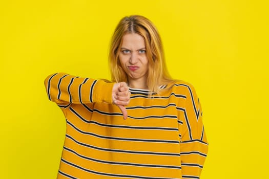 Dislike. Upset unhappy Caucasian woman showing thumbs down sign gesture, expressing discontent, disapproval, dissatisfied negative feedback. Dissatisfied girl indoors isolated on yellow background