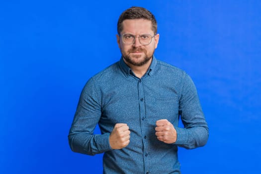 Upset frustrated annoyed Caucasian middle-aged man in glasses raising hands in indignant expression, quarreling, asking reason of conflict, why such stubborn. Adult guy isolated on blue background