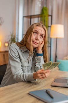 Caucasian mature woman freelancer counting dollar cash insufficient amount of money. Financial crisis. Bankruptcy. Poverty and destitution. Upset businesswoman with laptop sitting at home office table