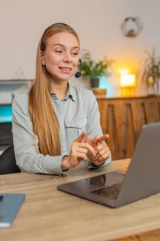Mature businesswoman wearing headset, freelance worker, call center or support service operator helpline, talking with client or colleague communication support. Girl using laptop at home office desk.