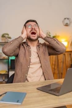 Caucasian young businessman freelancer shouting, trying not to hear the loud noise from neighbor apartment in building while they renovate home and he cant work on laptop netbook because of the noise.