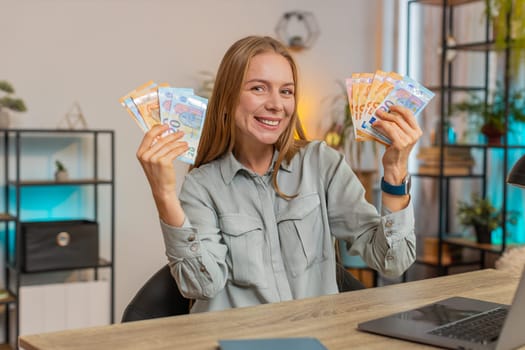 Mature businesswoman holding fan of cash money euro banknotes celebrate, dance, success career, lottery jackpot game winner, big income, wealth at home office workplace desk. Remote distant working.