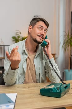 Caucasian man freelancer working, talking with client on retro old-fashioned wired telephone at home office table. Salesman in casual clothes. Remote distant job. Employment occupation. Vertical.