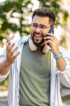 Angry adult Caucasian bearded man traveler arguing while talking on smartphone walking on the urban city street. Dissatisfied guy in glasses tourist shout into the phone, quarrels, expresses a problem