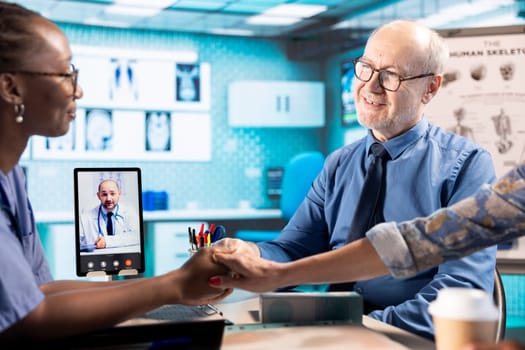 African american nurse doing comforting gesture for senior people on web call with specialist, holding hands with patients and encouraging them while they discuss with doctor remotely. Telemedicine.