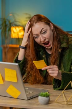 Tired exhausted frustrated Caucasian redhead business woman using laptop, sticky notes with many tasks, running late to work being in delay deadline, overworked multitasking. Girl freelancer. Vertical