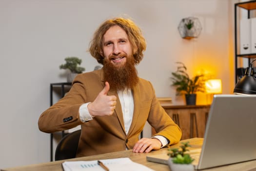 Like. Smiling Caucasian businessman looking approvingly at camera showing double thumbs up sign positive something good great news positive feedback. Redhead guy using laptop at home office table