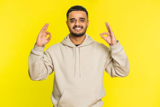 Keep calm down, relax, rest. Concentrated happy Indian man meditating breathes deeply with mudra yoga gesture, eyes closed, peaceful mind taking a break. Arabian Hindu guy on yellow background indoors