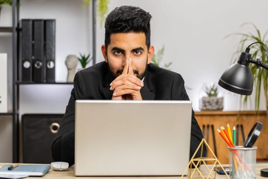 Portrait of Indian bearded businessman face freelancer at home office modern workplace working on laptop computer. Manager freelancer Arabian man works on notebook send messages makes online purchases