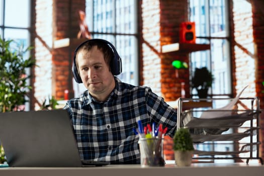 home office worker at desk using laptop, engaging in video call, participating in virtual meeting with colleagues. Man discussing with coworkers during videoconference meeting, using headset