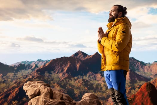 Pleased calm nature lover meditating on top of the mountain range, doing meditation poses and taking deep breaths for wellbeing and mental clarity. Peaceful zen hiker enjoys climbing.
