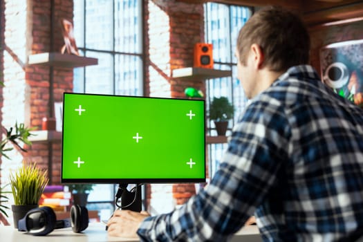 Employee seated at home office desk using green screen PC, checking emails displayed on screen, reading messages in inbox. Man managing electronic correspondence on mockup computer