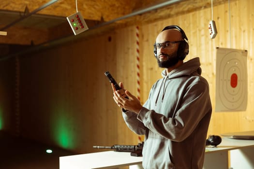 Person wearing safety gear reloading magazine into pistol during firearm practice session at indoor shooting range, learning safety practices. Arab man loading gun, doing self defense preparation