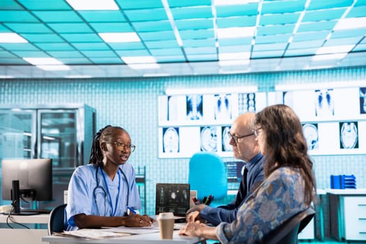 African american nurse evaluating lab test results and discussing potential recovery plan with senior couple, professional patient interaction at the facility. Examination results and analysis.