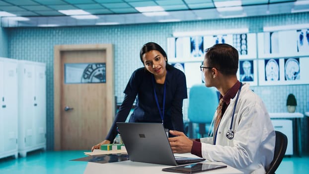 Indian professional medic sharing a high five with his nurse, medical expertise at a facility. Hospital staff reviewing x ray and MRI scan results and focusing on diagnostics report. Camera B.