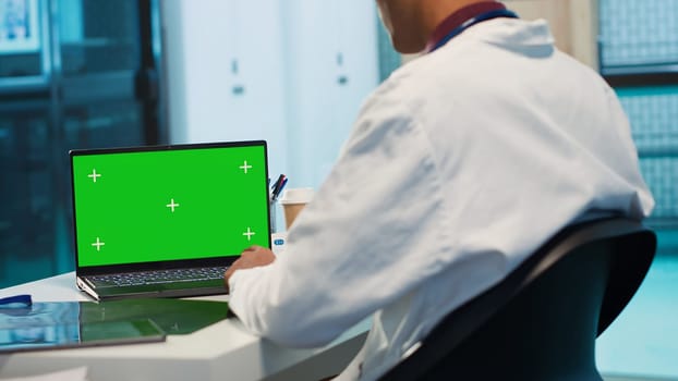 Indian physician works in his facility office next to chroma key, using modern technology for scan interpretation and results. Specialist offers professional advice based on records. Camera A.