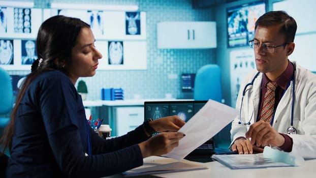 Indian healthcare expert sharing medical expertise with a patient in office, reviewing x ray scans and MRI diagnostics to focus on accurate treatment and recovery. Insurance consultation. Camera B.