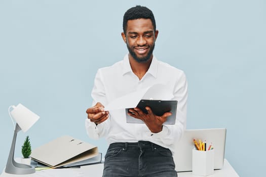 Happy man dressed in formal white shirt using tablet in a professional office setting, surrounded by office supplies and a laptop, positive mood, modern workspace, indoor shoot, business lifestyle concept.