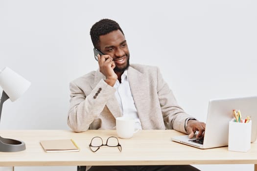 Happy professional man engaging in a phone call while using a laptop at his clean, organized workspace. The bright minimalistic setting highlights a productive work environment, suitable for remote work, business, and communication themes.