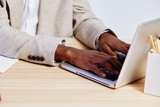 Image of a man working on a laptop in an office space, wearing a beige blazer and white shirt, with notepad and colored pencils on wooden desk. Concept: professional work, technology, productivity, business routine, modern workspace.