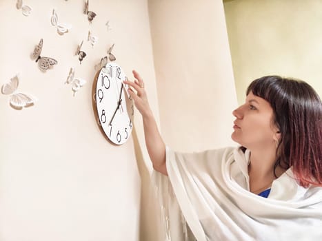Middle-aged woman psychologist adjusts a clock in her office, surrounded by decorative butterflies, focusing on her daily work routine.