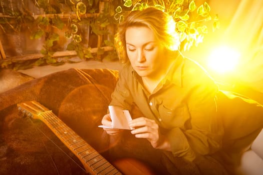 A musician is deeply focused on writing lyrics in a warm and inviting space filled with sunlight, surrounded by plants and a guitar.
