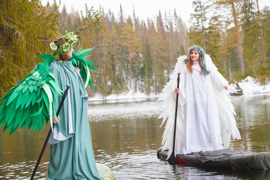 Two girls in white and green dresses role-play by a serene lake, embodying the encounter between winter and spring amidst nature's beauty.