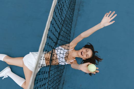 A lively young woman in sporty attire enjoying a game of tennis on a blue court, expressing excitement while reaching for a ball, capturing the essence of athleticism and joy