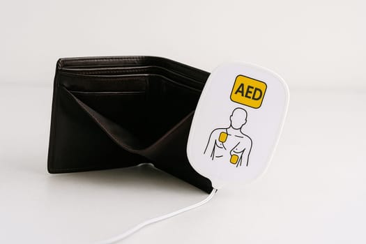 AI generated realistic empty men's wallet with emergency AED defibrillator pads symbolizing financial crisis and urgent economic recovery white background money rescue metaphor