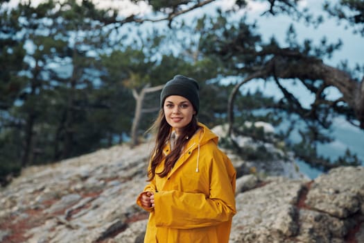A woman in a yellow raincoat enjoying the breathtaking view from the top of a mountain surrounded by lush trees Travel adventure in nature