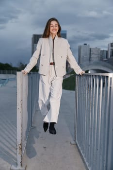 A confident woman dressed in a light-colored business outfit, smiling and posing outdoors against a city skyline, embodies modern professionalism and empowerment.