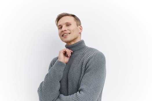 Happy man wearing a cozy gray turtleneck sweater, smiling and looking away thoughtfully, standing against a plain white background. The image emphasizes comfort, warmth, and a relaxed mood, suitable for lifestyle themes.