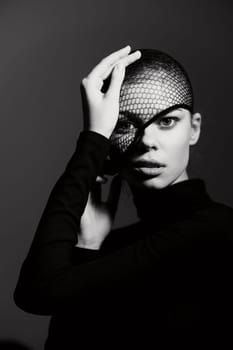 Stunning model with a shaved head wearing a netted veil and black long-sleeve top. The high-contrast dark background emphasizes her artistic expression and unique style.