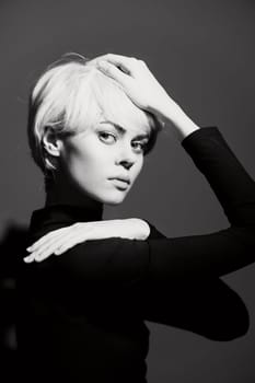 A fashionable woman with short, pale hair poses in a subtle yet expressive manner. The black-and-white setting highlights her striking features and sophisticated aura.