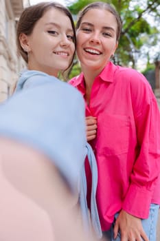 Caucasian women smiling closely while taking a selfie together on a city street. Outdoor setting with trees and buildings, capturing a joyful and candid moment of friendship and connection .Vertical