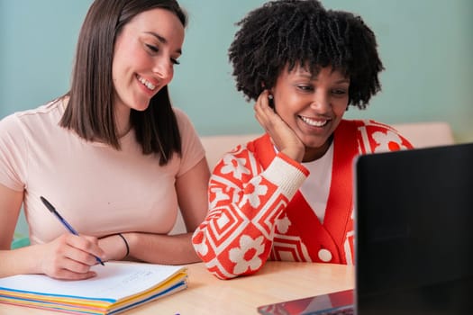 Caucasian and African American students work together using a laptop and notebook. Focused and cheerful, they collaborate in a cozy indoor space, representing learning, diversity, and teamwork.