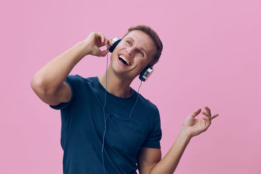Joyful young man in casual attire, listening to music with headphones, expressing happiness and excitement, with vibrant pink background, capturing a moment of relaxation and fun, studio shot. Concept: music enjoyment