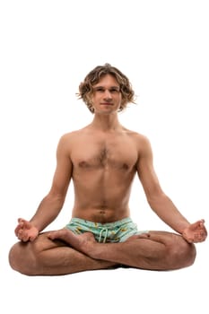 Full body barefoot young male in shorts with naked torso sitting in Padmasana pose and meditating during yoga session against white background