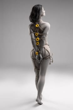 Full body back view of unrecognizable naked female tied with ropes with yellow flowers standing against white background