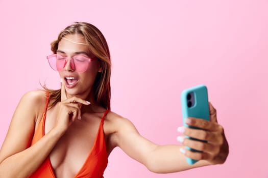 Vibrant and fun a young woman in a swimsuit capturing the perfect selfie moment on a pink background