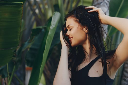 Woman with wet hair standing in front of a palm tree with hands on head, tropical vacation concept
