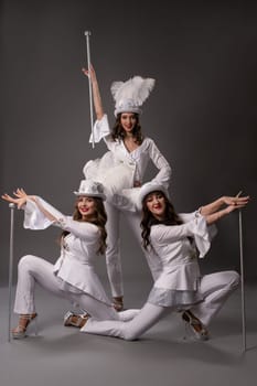 Full body of happy young multiracial women in white clothes and protective masks smiling and looking at camera while sitting against black background