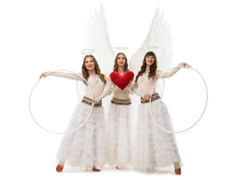 Full body of female dancer in stylish angel outfits with wings and halos looking at camera with hoops and heart against white background