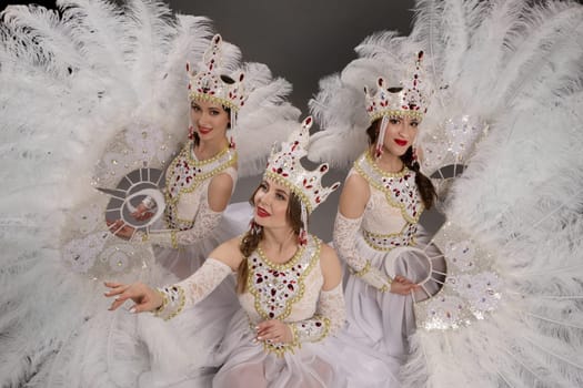 Top view of group of cheerful young women in white dresses and decorative deer horns while sitting on floor with crossed legs