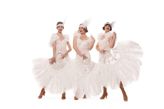 Full body of content female dancers in white art deco costumes with headband looking at camera with feather fans against white background