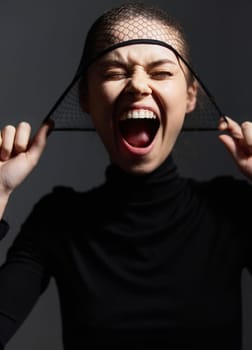 Excited female figure showing a wide smile and laughter while holding a fishnet headpiece, symbolizing freedom and joy. Dark and dramatic setting enhances emotion.